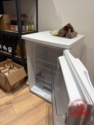 un petit réfrigérateur dans un coin d'une pièce où se trouvent des cartons par terre