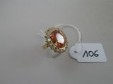 une image représentant une bague ornée d'une grosse pierre orange entourée de petits diamants blancs