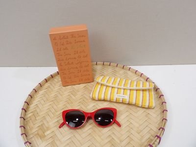 un plateau en paille sur lequel sont posés des lunettes de soleil, un livre et une paire de lunettes de soleil