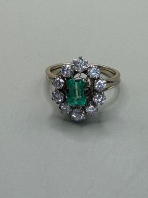 an emerald and diamond cluster ring on a white surface