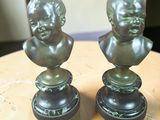 paire de bustes d'enfants en bronze sur socle, posés sur une table en bois