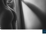 black and white photograph of a naked woman standing in front of a window