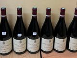 six bottles of wine are lined up on a wooden shelf