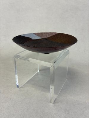 un présentoir en acrylique transparent surmonté d'un bol, posé sur une surface blanche