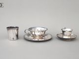 une tasse et une soucoupe en argent posées l’une à côté de l’autre
