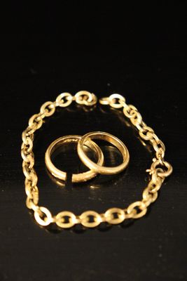 two gold wedding rings and a chain bracelet on a black surface