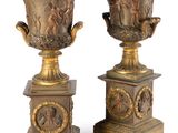 pair of antique bronze vases with figures on pedestals on a white background