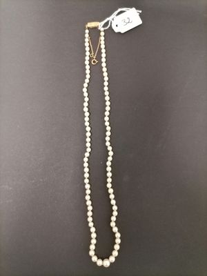 a white pearl necklace with a gold clasp on a black background