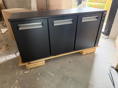 two black refrigerators sitting on top of pallets in a room