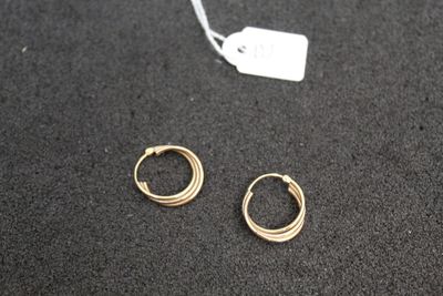 two pairs of gold hoop earrings sitting on top of a black surface
