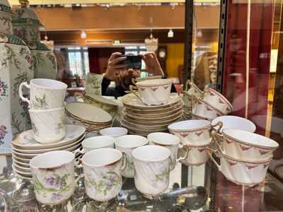 une femme en train de prendre une photo d'un présentoir de tasses et soucoupes en porcelaine