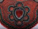 a close up of a beaded necklace with a red stone in the center