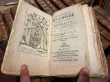 une personne tient un vieux livre à la main devant une pile de vieux livres