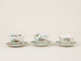 three cups and saucers with birds on them on a white surface