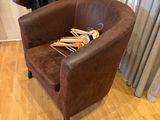 a brown chair with a book on it in front of a window