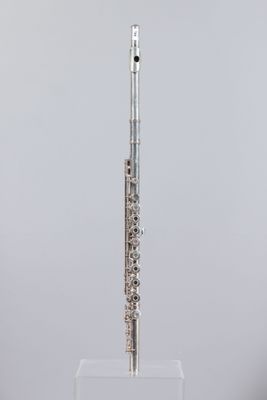 a silver flute on a clear stand against a gray background