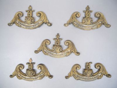 quatre poignées de tiroir en laiton vieilli, ornées de motifs élaborés, sur un fond blanc