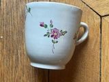 a white cup with pink flowers on it sitting on a wooden floor