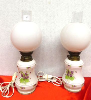 pair of white lamps with purple flowers on them sitting on a red cloth