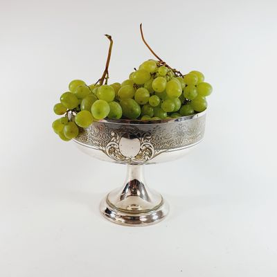 a silver bowl with grapes in it on a white surface