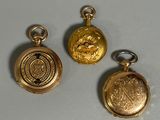 three gold pocket watches are sitting on a white surface