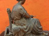 statue en bronze d'une femme assise sur une chaise avec un instrument de musique