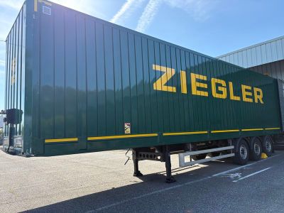 une semi-remorque verte arborant un logo Ziegler jaune, garée devant un immeuble
