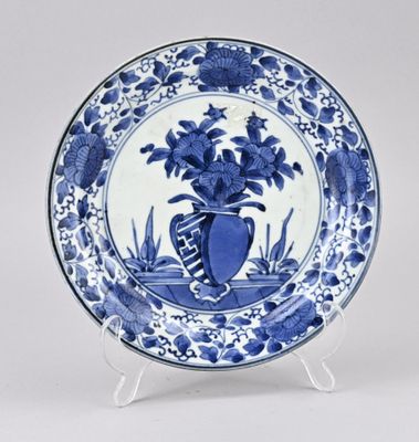 une assiette bleue et blanche sur laquelle est représenté un vase de fleurs