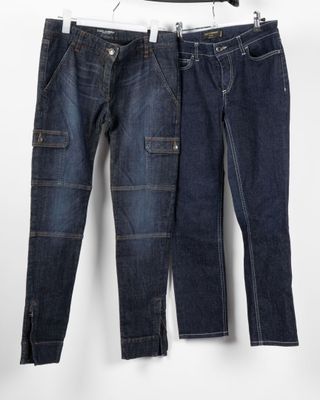 two pairs of jeans hanging on a hanger in front of a white wall