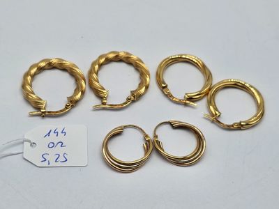 quatre paires de boucles d'oreilles créoles en or et une étiquette de prix posée sur une surface blanche