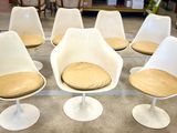 six white tulip chairs with tan cushions sit in a room