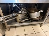 Des casseroles et des poêles sont posées sur une étagère en acier inoxydable dans une cuisine
