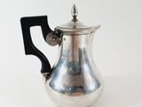 an antique silver tea pot with a black handle on a white background