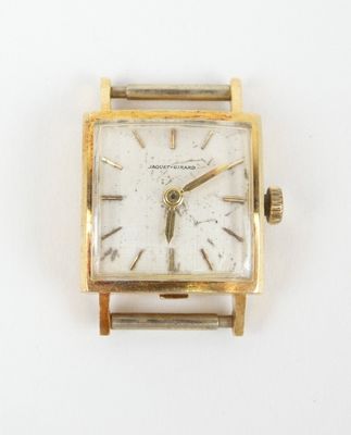 une montre en or avec un cadran blanc posée sur une surface blanche