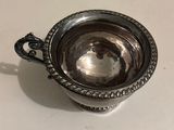 an antique silver cup with a handle on a white table