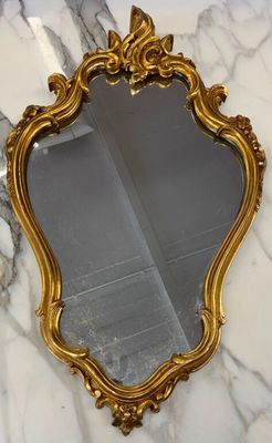 un miroir au cadre doré ouvragé posé sur un plan de travail en marbre