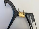 une sculpture de cheval en métal posée sur un socle en bois, elle-même posée sur une table