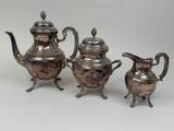 two silver teapots and a coffee pot sitting on a table