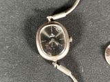 a silver wrist watch sitting next to a coin