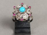 un gros plan d'une bague ornée d'une turquoise entourée de pierres roses et blanches