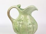un vase vert muni d'une anse sur fond blanc