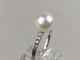 a close up of a pearl and diamond ring on a clear surface