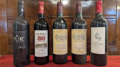 six bottles of wine are lined up on a red table cloth