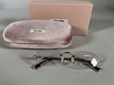 une paire de lunettes dans un étui rose, posée sur une surface grise avec sa boîte