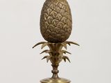 lampe de table en forme d'ananas en laiton, posée sur un socle en bois, sur fond blanc