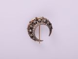 Gros plan sur une broche en forme de croissant en or, sertie de diamants noirs et blancs
