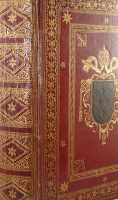 un vieux livre rouge aux tranches dorées, orné d'un blason sur la couverture