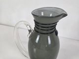 a glass pitcher with a handle on a white surface