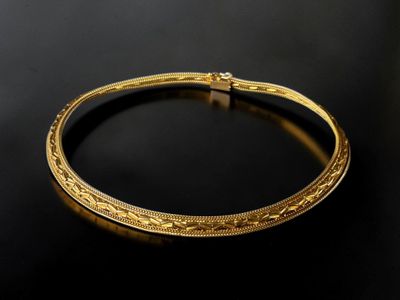 a gold bangle with intricate design on a black surface