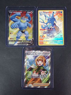 Trois cartes Pokémon différentes sont posées sur une surface noire